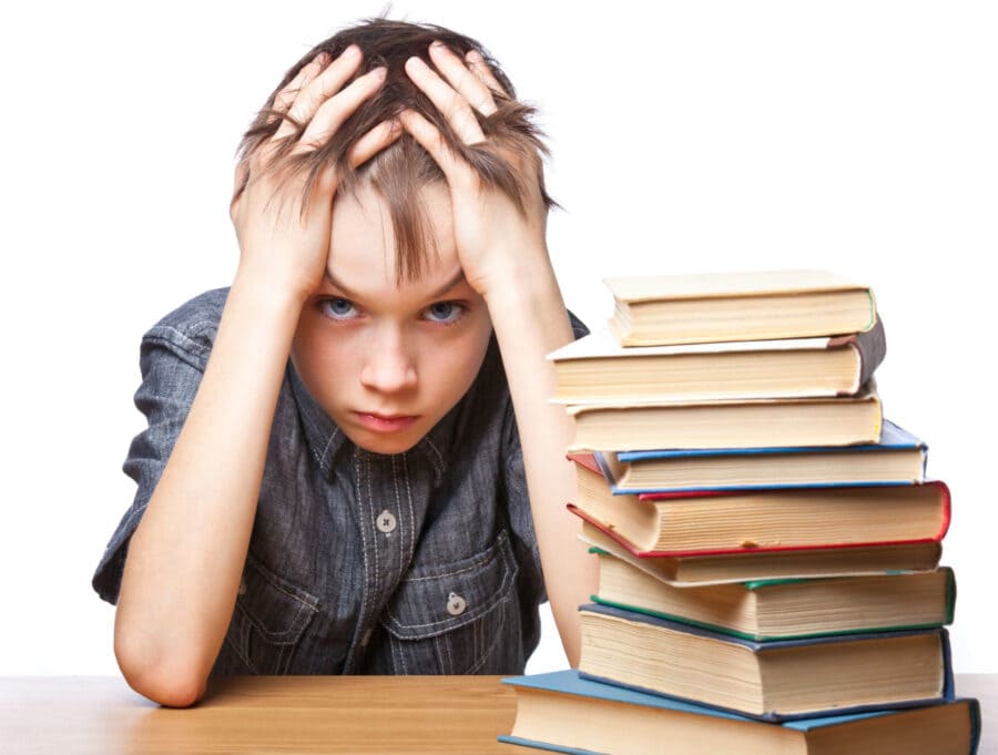 Zmęczony chłopiec trzyma się za głowę przed stosem grubych książek